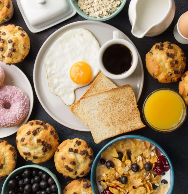 A variety of breakfast items, including pancakes, scrambled eggs, croissants, and a cup of coffee, arranged on a rustic table to represent the breakfast category