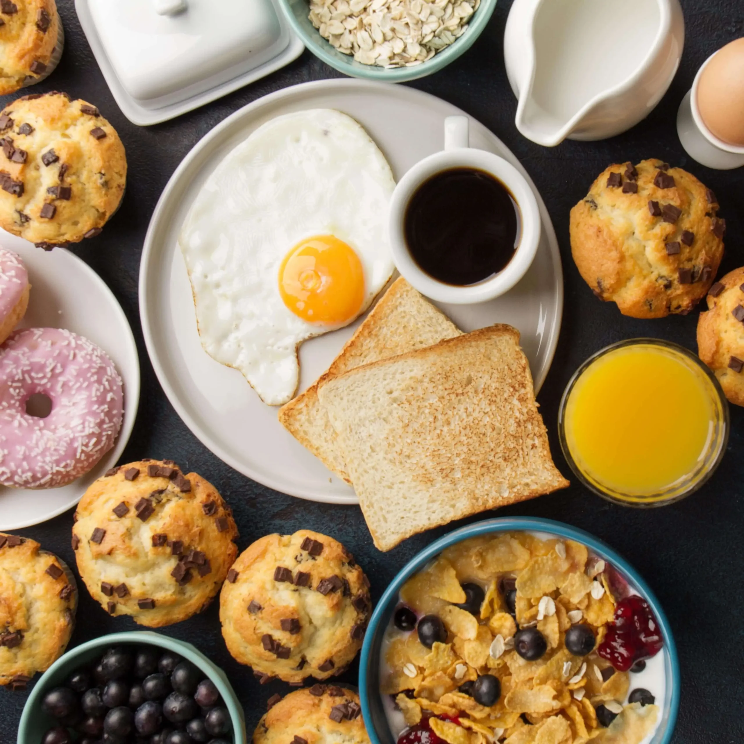 A variety of breakfast items, including pancakes, scrambled eggs, croissants, and a cup of coffee, arranged on a rustic table to represent the breakfast category